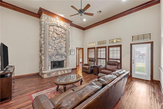 living room with dark wood-type flooring, ornamental molding, a stone fireplace, and ceiling fan