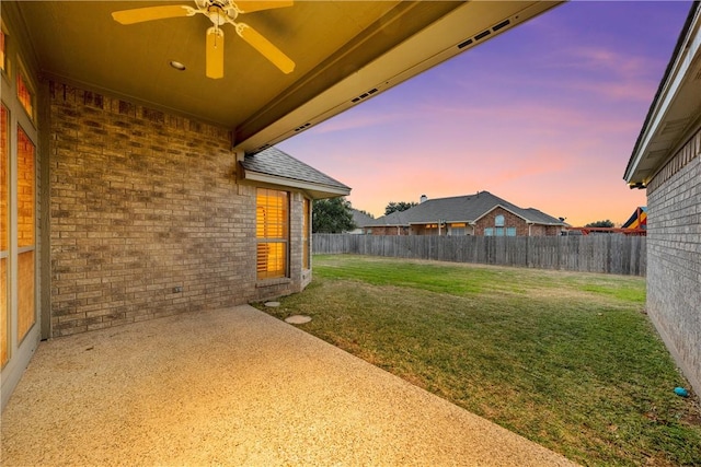 yard at dusk featuring ceiling fan and a patio area