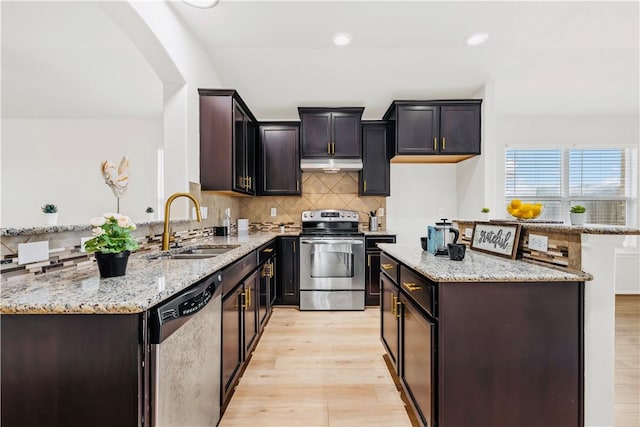 kitchen with light wood-type flooring, light stone countertops, sink, and appliances with stainless steel finishes