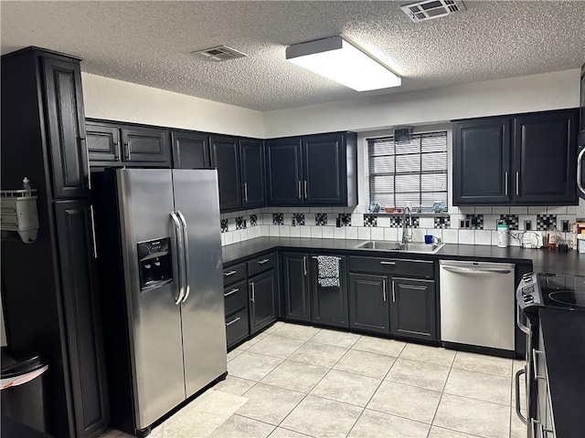 kitchen featuring sink, tasteful backsplash, a textured ceiling, light tile patterned floors, and appliances with stainless steel finishes