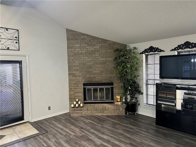 unfurnished living room featuring hardwood / wood-style floors, lofted ceiling, and a brick fireplace