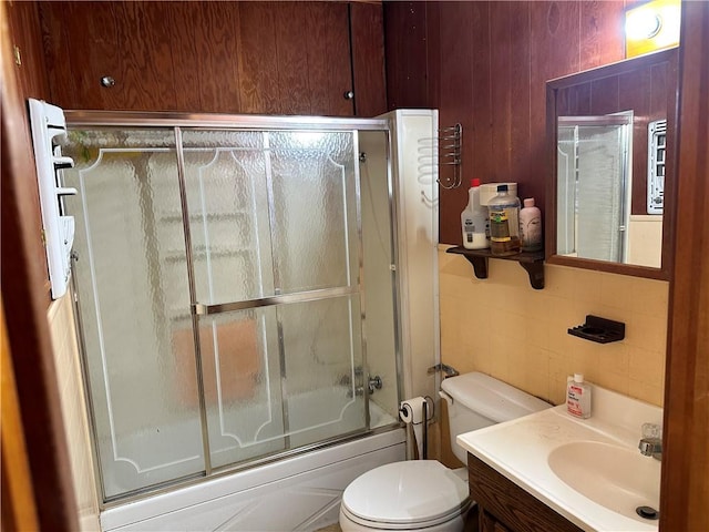 full bathroom with toilet, combined bath / shower with glass door, tile walls, and vanity