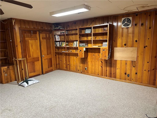 interior space featuring carpet flooring, wooden walls, and ceiling fan