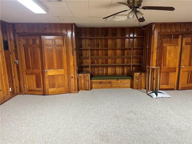 interior space with light colored carpet, ceiling fan, and wood walls