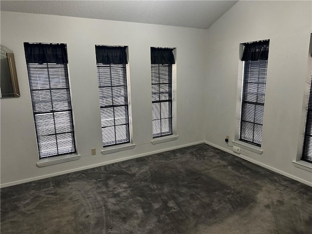 unfurnished room featuring plenty of natural light, lofted ceiling, and dark colored carpet