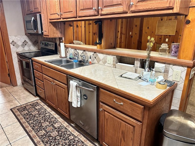 kitchen featuring appliances with stainless steel finishes, tasteful backsplash, sink, light tile patterned floors, and tile counters