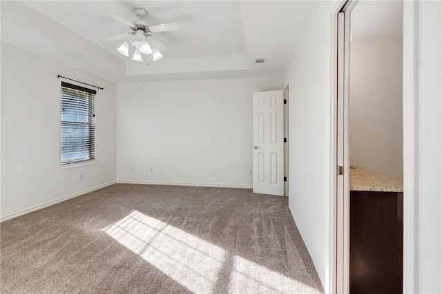 carpeted empty room featuring a raised ceiling and ceiling fan