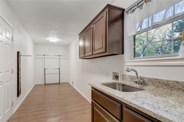 kitchen featuring dark brown cabinets, light hardwood / wood-style floors, light stone countertops, and sink