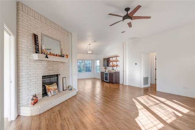 unfurnished living room featuring ceiling fan, a brick fireplace, wine cooler, light hardwood / wood-style flooring, and lofted ceiling