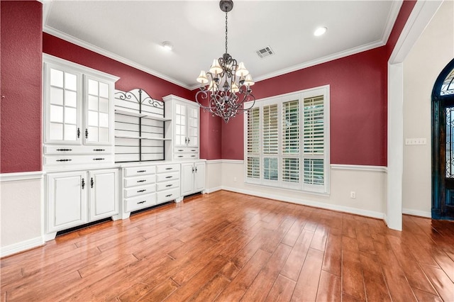 unfurnished dining area featuring plenty of natural light, light hardwood / wood-style floors, crown molding, and an inviting chandelier