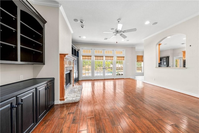 unfurnished living room featuring ceiling fan, wood-type flooring, ornamental molding, and a high end fireplace