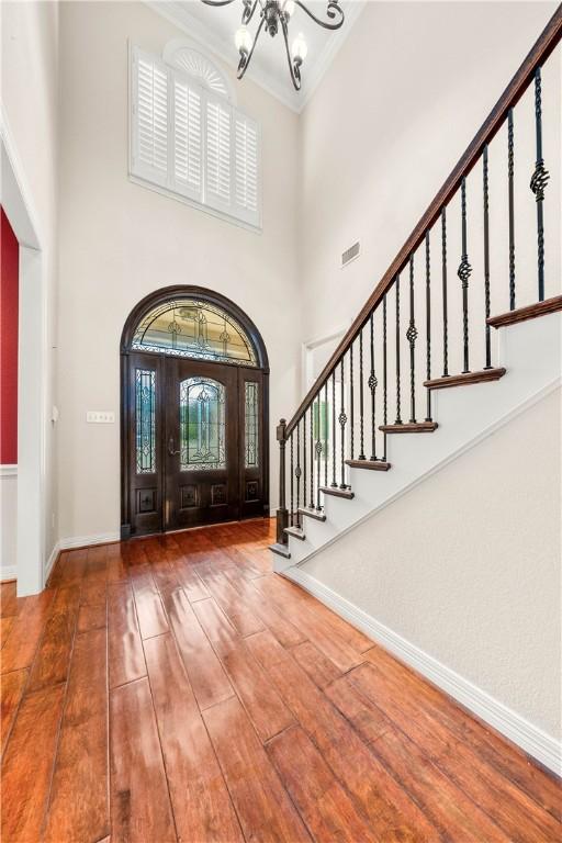 entryway with hardwood / wood-style floors, a towering ceiling, a chandelier, and ornamental molding