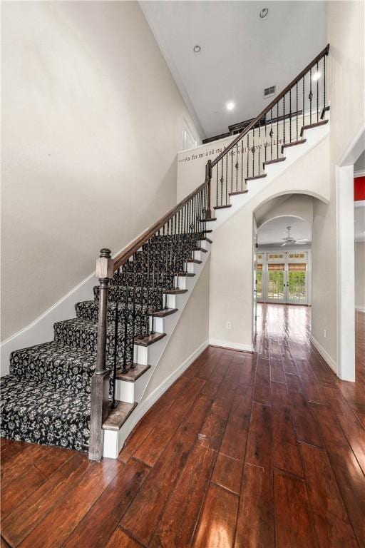 staircase with wood-type flooring, a towering ceiling, and ceiling fan