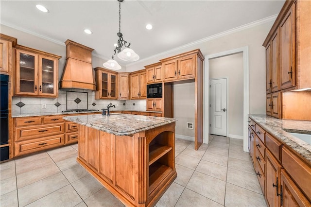 kitchen with light stone countertops, hanging light fixtures, a center island with sink, black appliances, and custom range hood