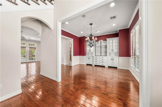 empty room with dark wood-type flooring, ceiling fan with notable chandelier, and ornamental molding