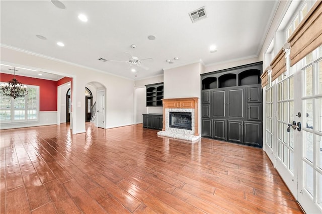 unfurnished living room with wood-type flooring, ceiling fan with notable chandelier, and ornamental molding