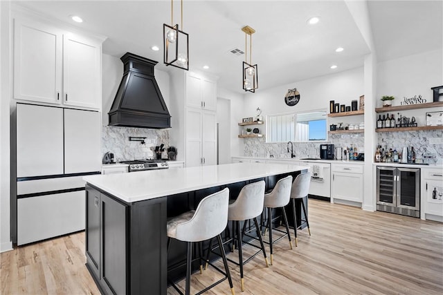 kitchen with light hardwood / wood-style floors, custom exhaust hood, beverage cooler, white cabinets, and white fridge