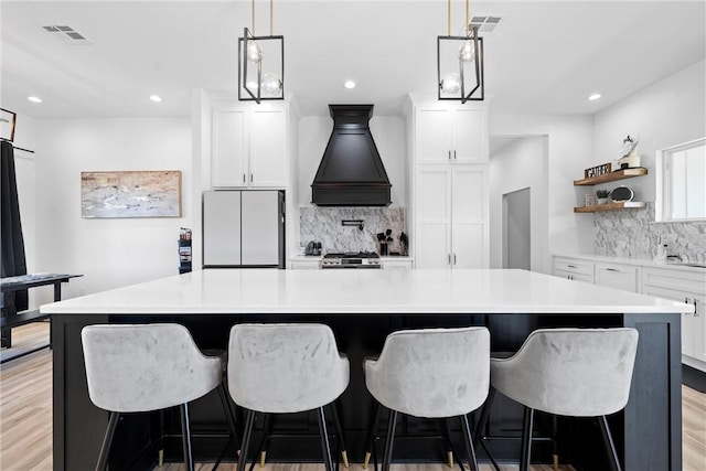 kitchen with white cabinets, custom range hood, white refrigerator, and a large island