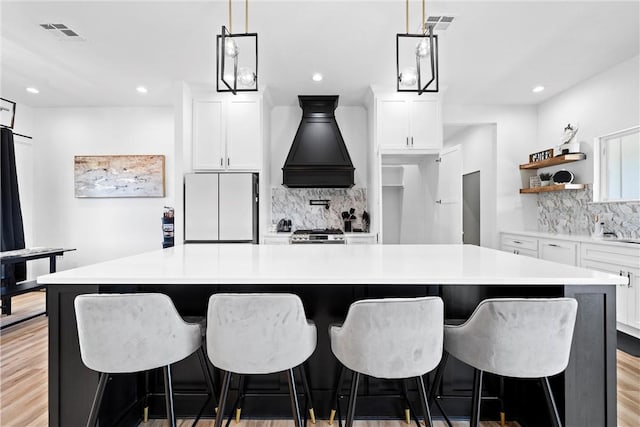 kitchen with white refrigerator, white cabinetry, a large island, light hardwood / wood-style floors, and custom range hood