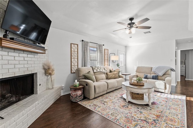 living room featuring ceiling fan, dark hardwood / wood-style flooring, and a brick fireplace