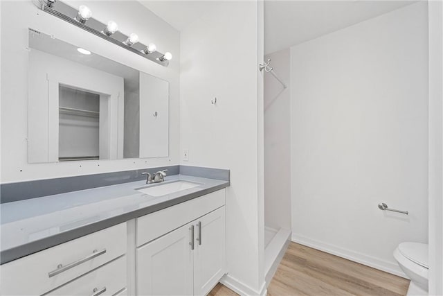 bathroom with wood-type flooring, vanity, toilet, and walk in shower