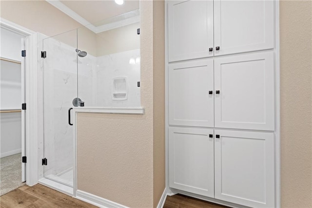 bathroom featuring wood-type flooring, ornamental molding, and a shower with shower door