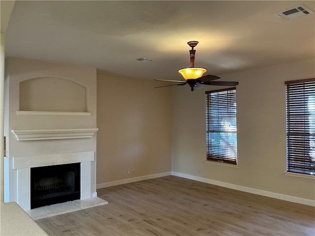 unfurnished living room featuring hardwood / wood-style floors, ceiling fan, a wealth of natural light, and a tiled fireplace