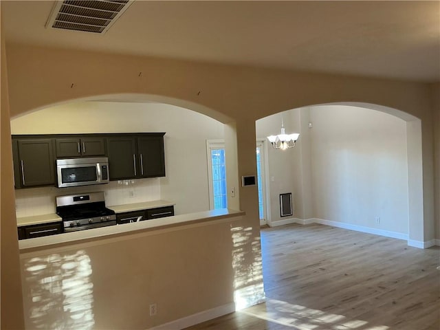 kitchen with light hardwood / wood-style flooring, a chandelier, decorative light fixtures, decorative backsplash, and appliances with stainless steel finishes