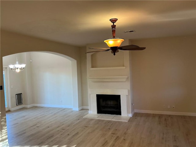 unfurnished living room with ceiling fan with notable chandelier, a fireplace, and light hardwood / wood-style flooring