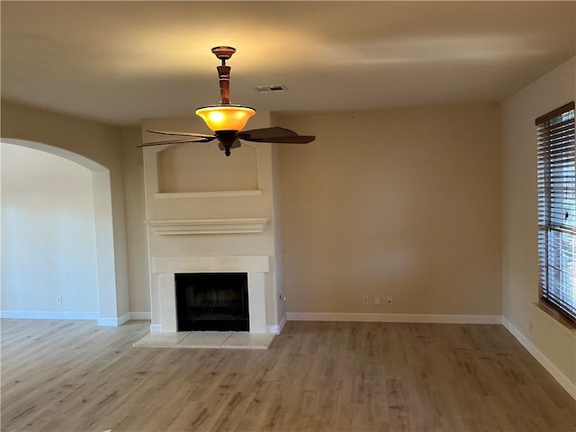 unfurnished living room featuring hardwood / wood-style flooring, ceiling fan, and a tiled fireplace