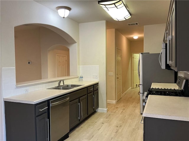 kitchen featuring decorative backsplash, appliances with stainless steel finishes, kitchen peninsula, sink, and light hardwood / wood-style floors