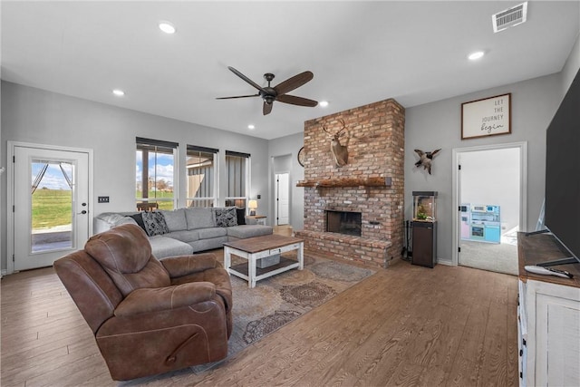 living room featuring ceiling fan, light hardwood / wood-style flooring, and a brick fireplace