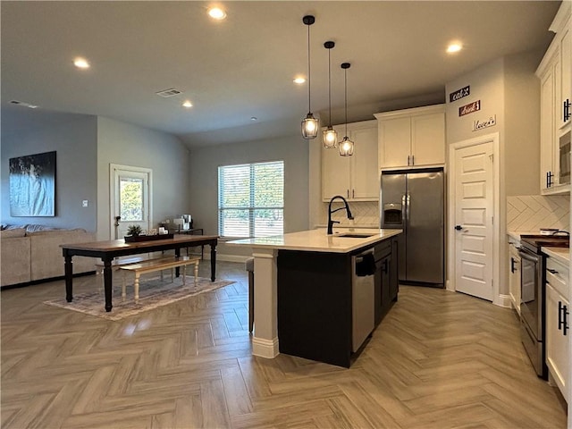 kitchen with white cabinets, stainless steel appliances, light parquet floors, and an island with sink