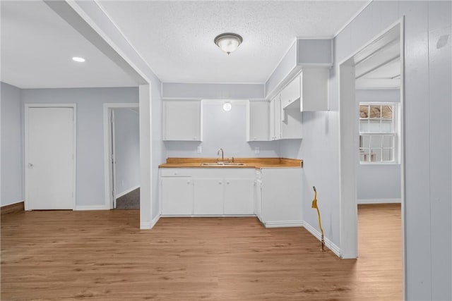 kitchen featuring white cabinets, sink, light hardwood / wood-style flooring, a textured ceiling, and butcher block counters