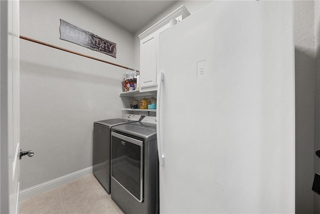 laundry area with washing machine and clothes dryer, light tile patterned floors, and cabinets