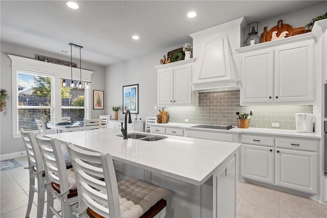 kitchen with custom exhaust hood, a center island with sink, sink, hanging light fixtures, and white cabinetry