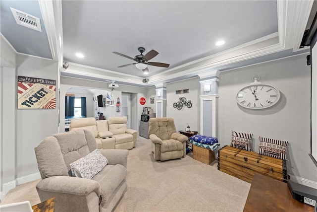 carpeted living room with a raised ceiling, ceiling fan, crown molding, and ornate columns