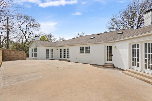 back of house with entry steps, a patio, brick siding, french doors, and a chimney