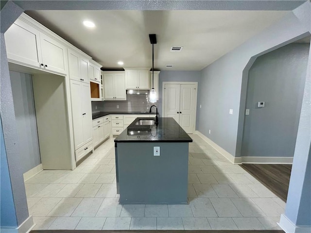 kitchen with white cabinets, sink, decorative backsplash, an island with sink, and light tile patterned flooring