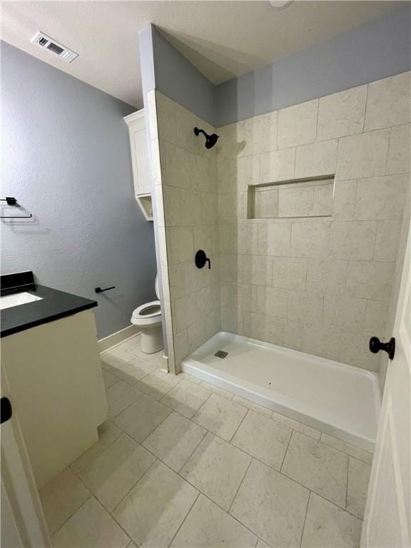 bathroom featuring tile patterned flooring, a tile shower, vanity, and toilet