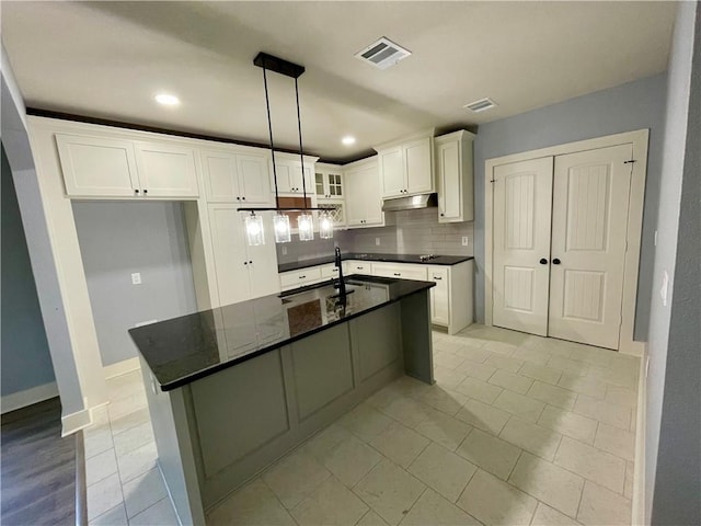 kitchen featuring backsplash, a kitchen island with sink, white cabinets, sink, and decorative light fixtures