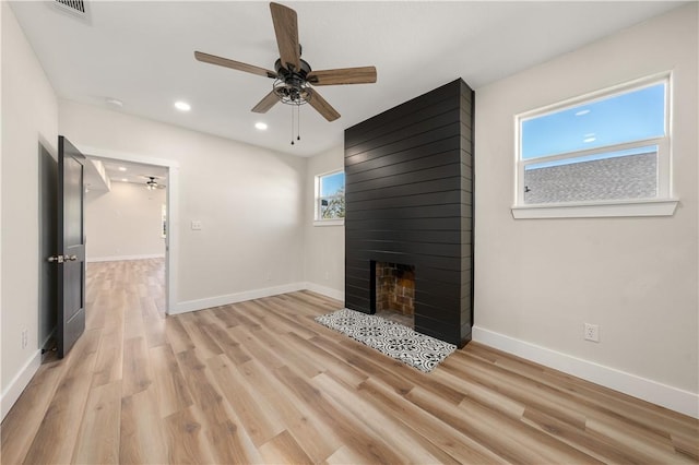 unfurnished living room featuring a large fireplace, light hardwood / wood-style flooring, and ceiling fan