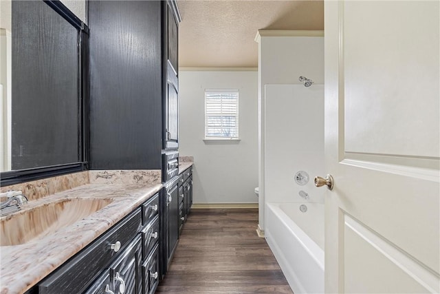 full bathroom featuring toilet, ornamental molding, wood finished floors, a textured ceiling, and vanity