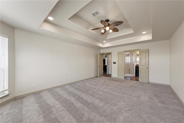 carpeted empty room featuring a tray ceiling, plenty of natural light, visible vents, and baseboards