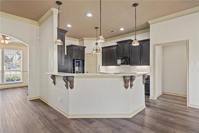 kitchen featuring arched walkways, black microwave, dark wood-style flooring, and a kitchen breakfast bar