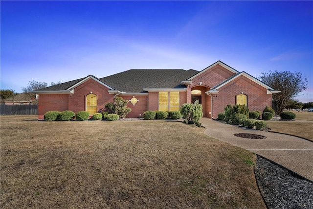 single story home featuring a front lawn, a shingled roof, fence, and brick siding