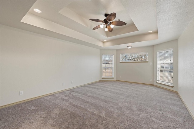 carpeted spare room with ceiling fan, baseboards, a raised ceiling, and a wealth of natural light