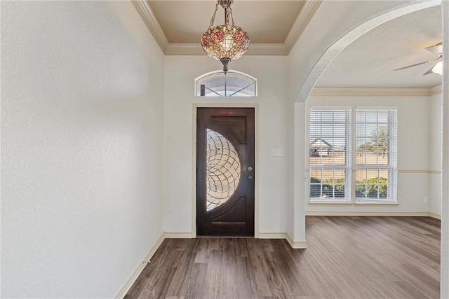 entryway featuring arched walkways, crown molding, dark wood-type flooring, a ceiling fan, and baseboards