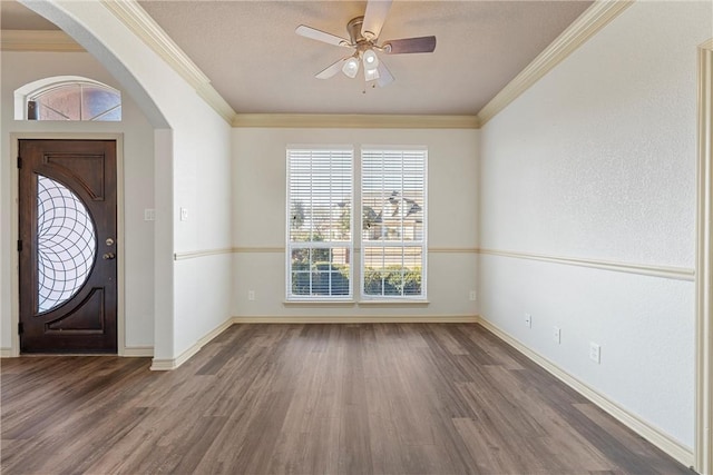 entrance foyer featuring baseboards, ornamental molding, arched walkways, and wood finished floors