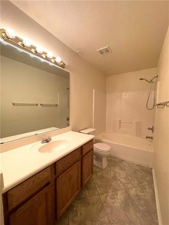 full bathroom featuring tile patterned floors, a textured ceiling, toilet, shower / washtub combination, and vanity